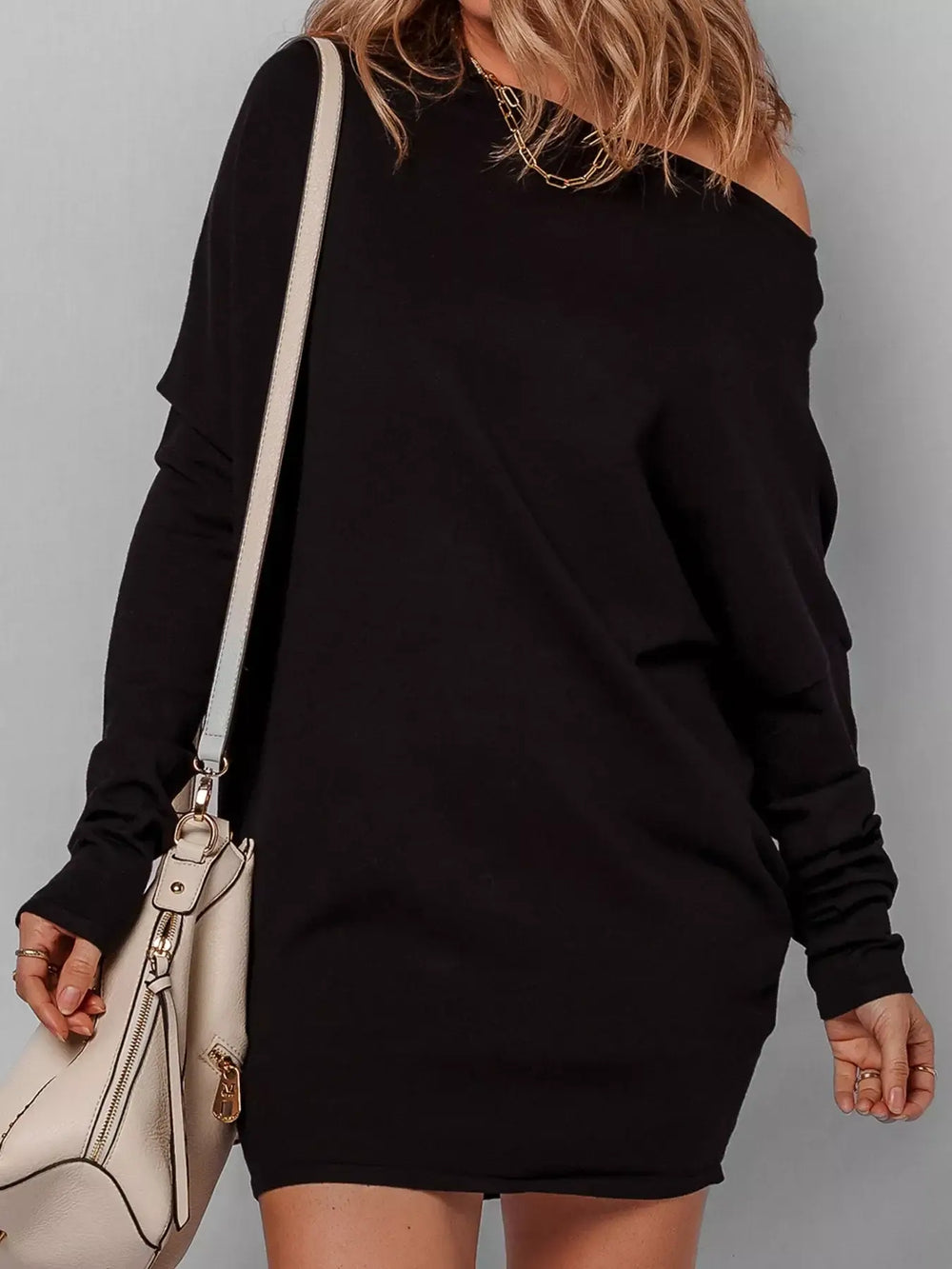 Model wearing black asymmetric batwing sweater dress with handbag, showcasing off-shoulder style and batwing sleeves.