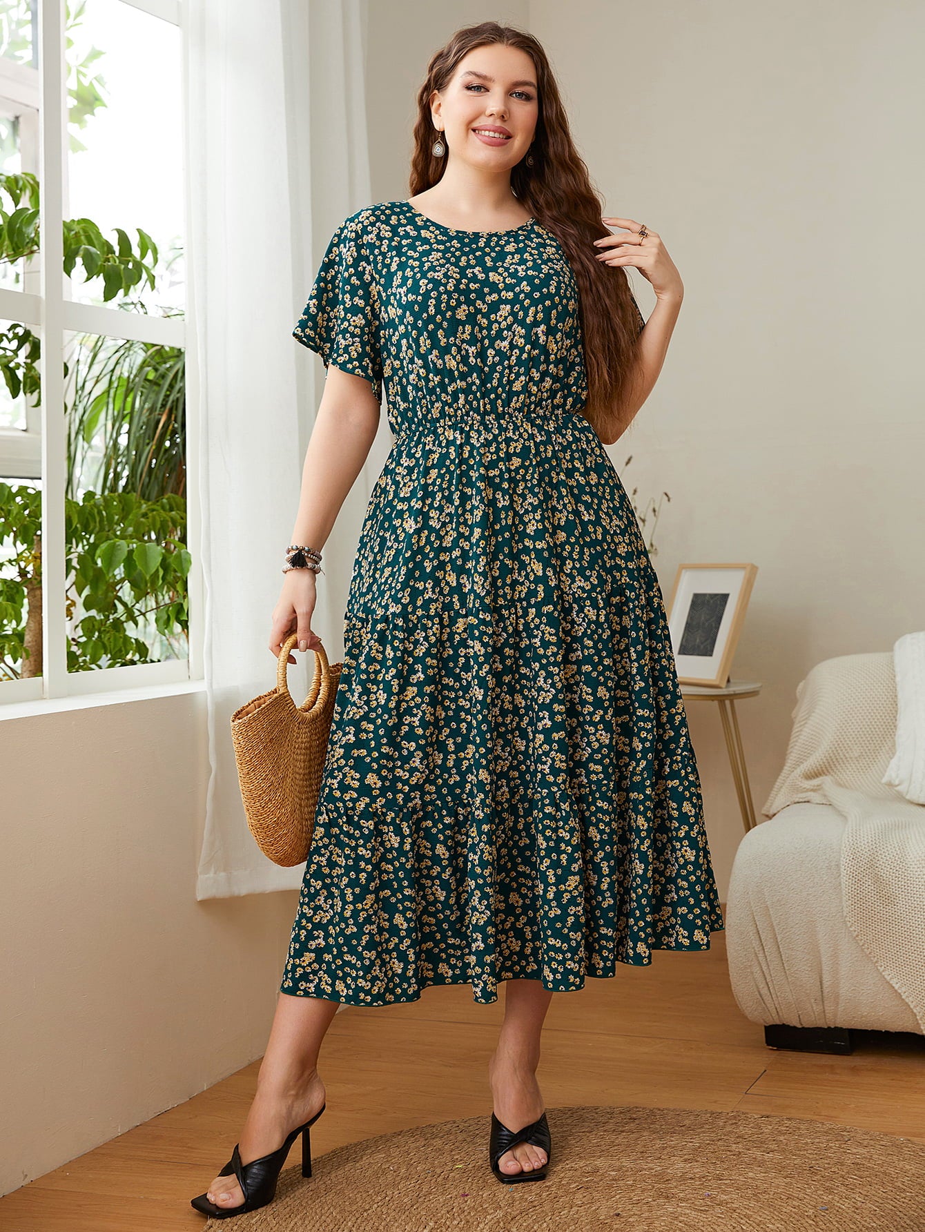 Woman wearing Floral Midi Dress with round neck and flutter sleeves, holding a straw bag, standing in a bright room.