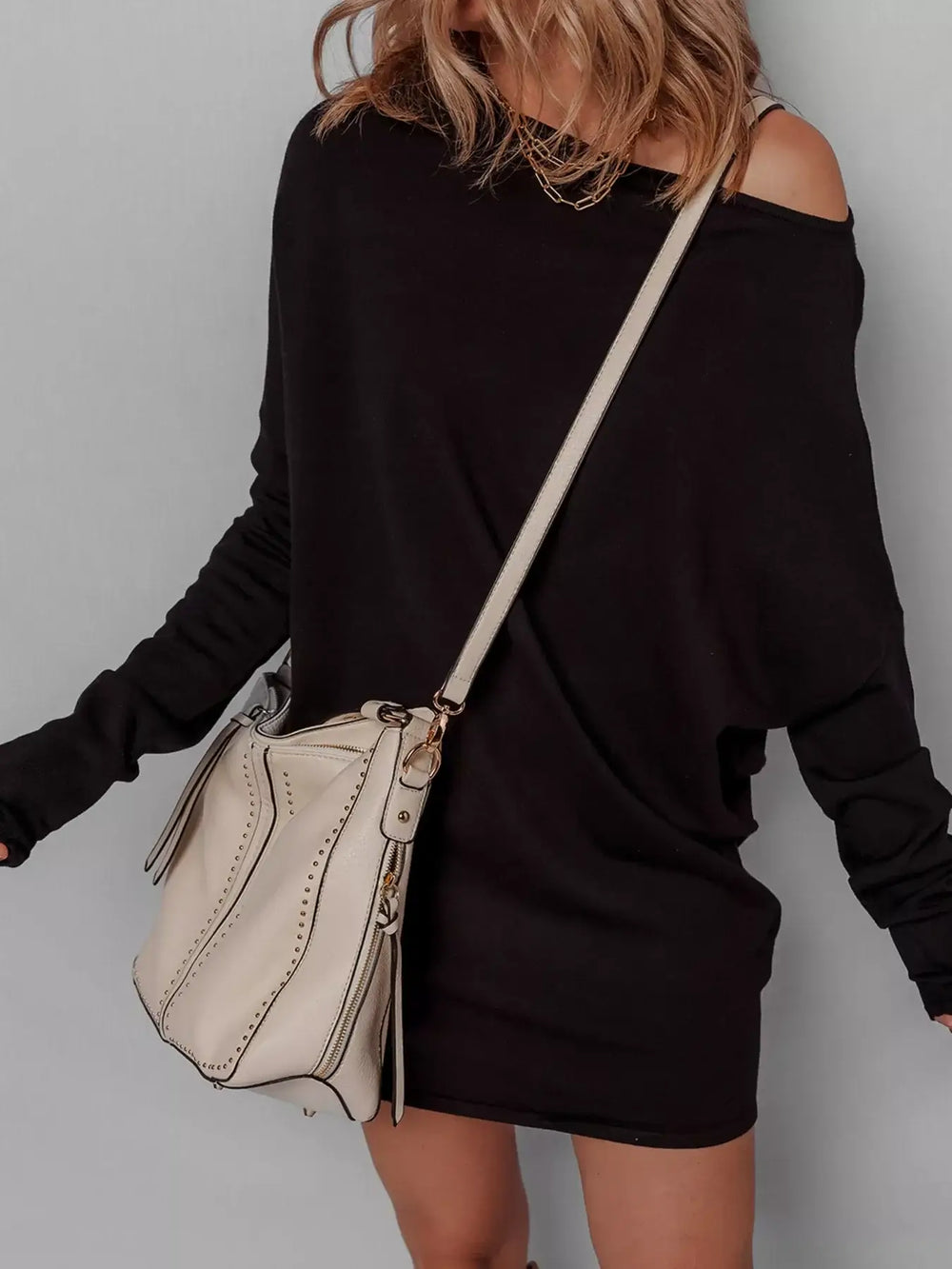 Woman wearing an asymmetric batwing sweater dress with a beige handbag. Features basic style and slight stretch. Perfect for casual outings.