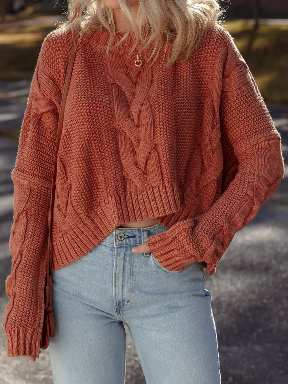 Woman wearing Cable Knit Sweater with chunky slouchy fit and textured design in a warm outdoor setting.