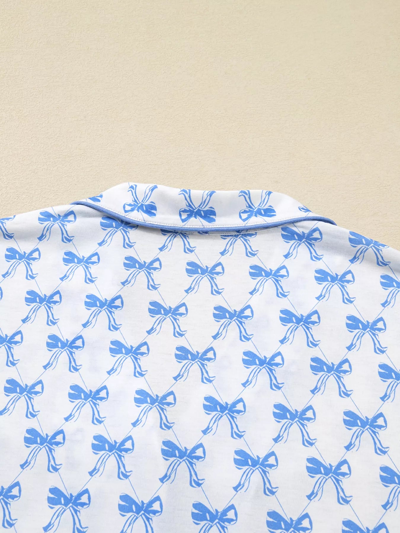 Close-up of Bow Print Pajama Set long sleeve shirt from Felvior, featuring blue bow patterns on white fabric.