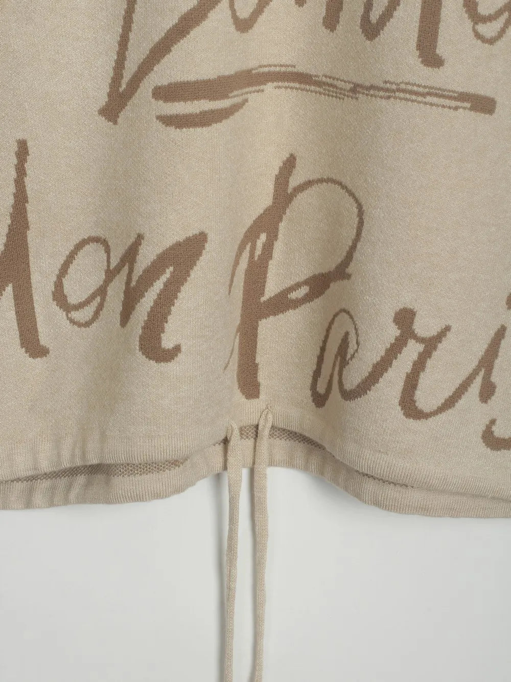 Close-up of a Letter Pattern Sweater with a drawstring hem and script design. Features modern style and relaxed fit.