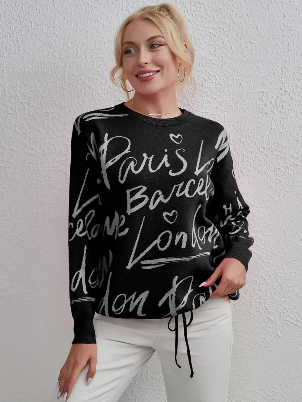 Woman wearing black Letter Pattern Sweater with drawstring hem and dropped shoulders, featuring city names in white lettering.